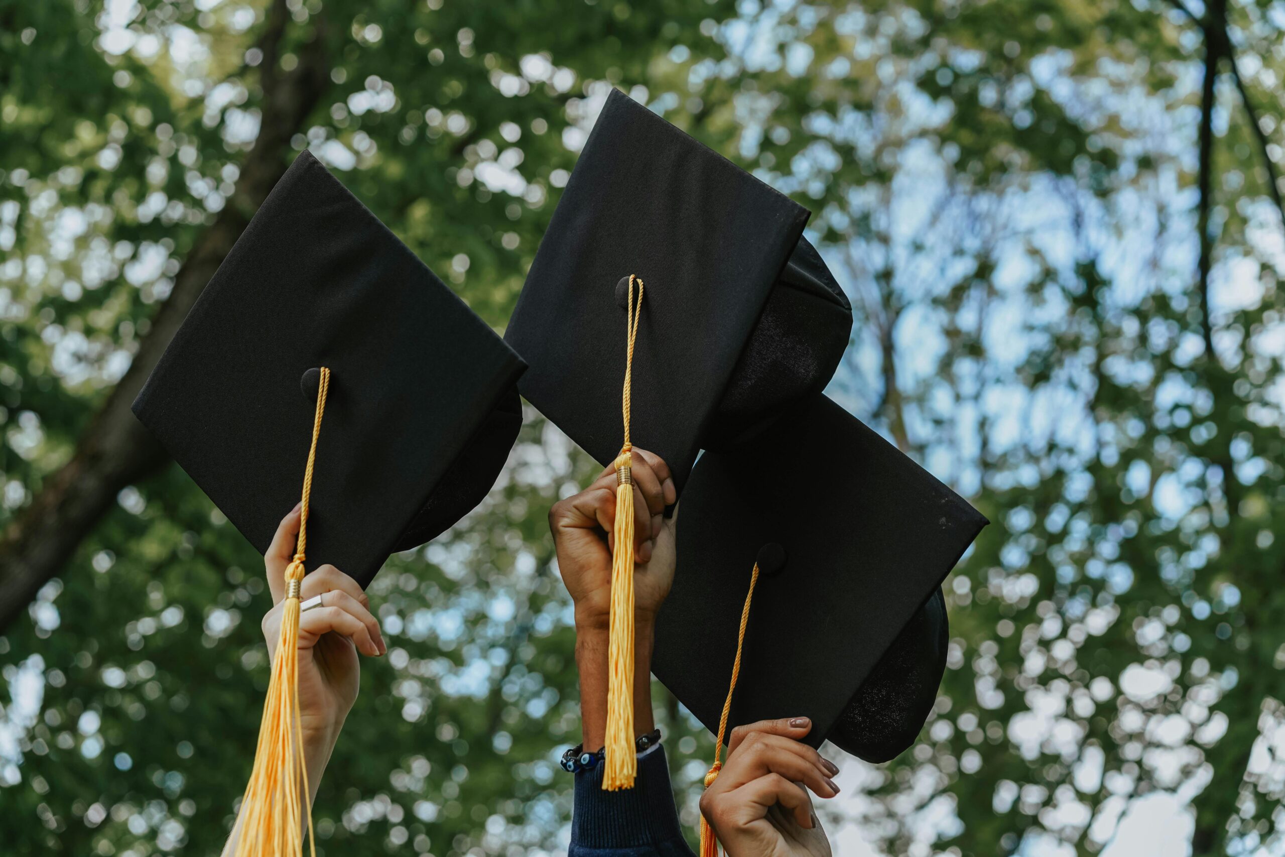 Three hands holding graduation caps in celebration, symbolizing success.