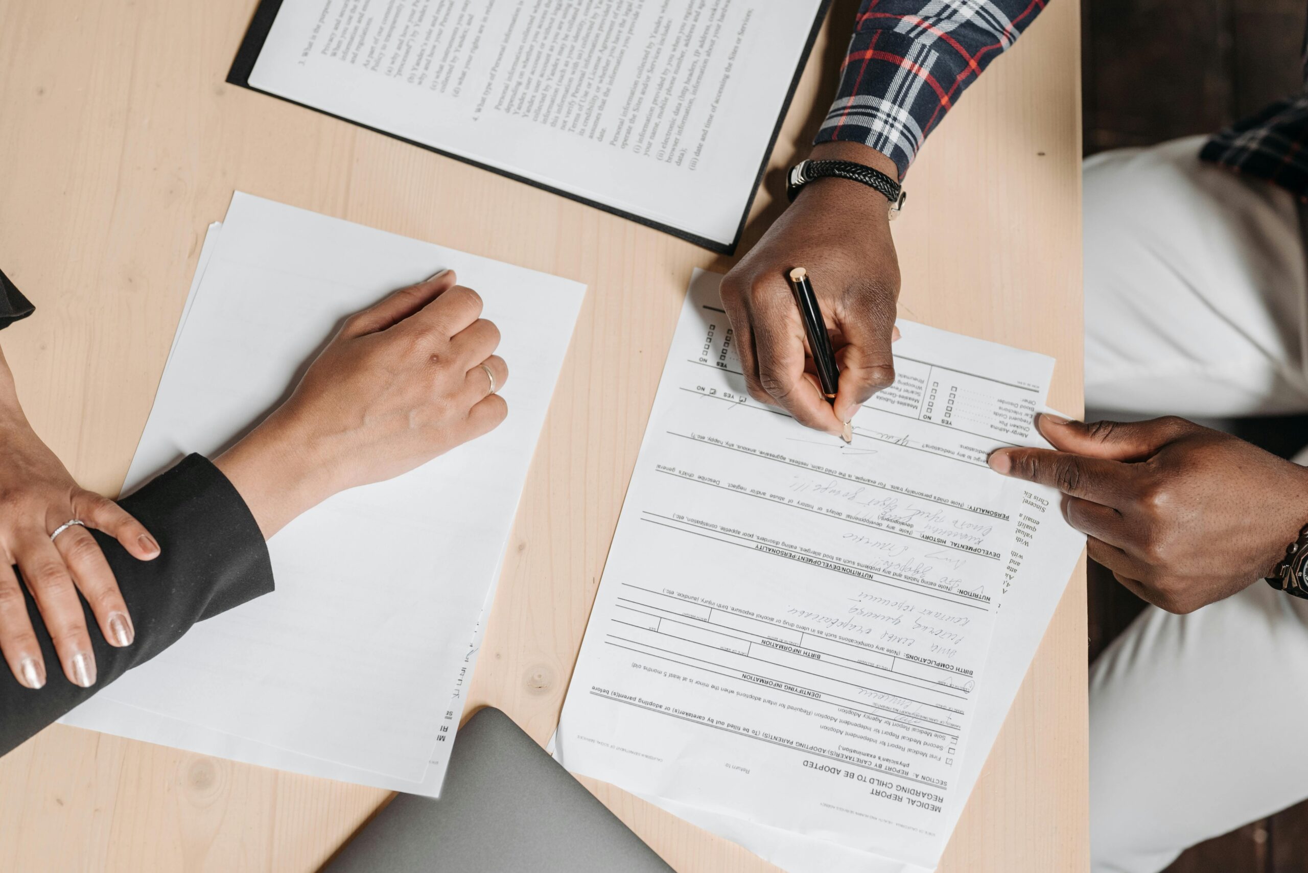 Close-up of two people signing documents at an office desk, depicting business collaboration.